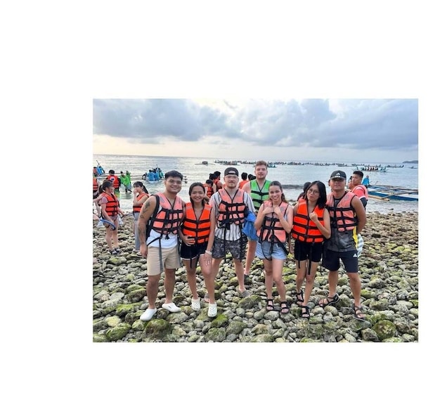 A group of people on a rocky beach with boats in the background. 4