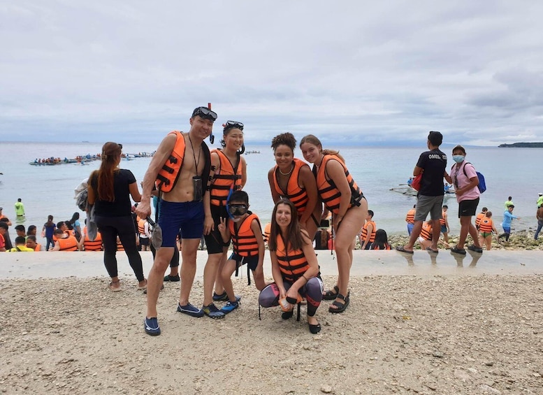 A group of people wearing life jackets on a beach with boats in the background. 5