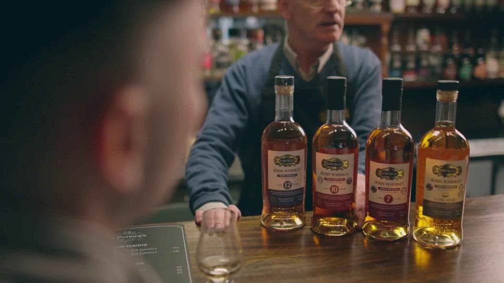 A person at a bar with four bottles of Irish whiskey. 5