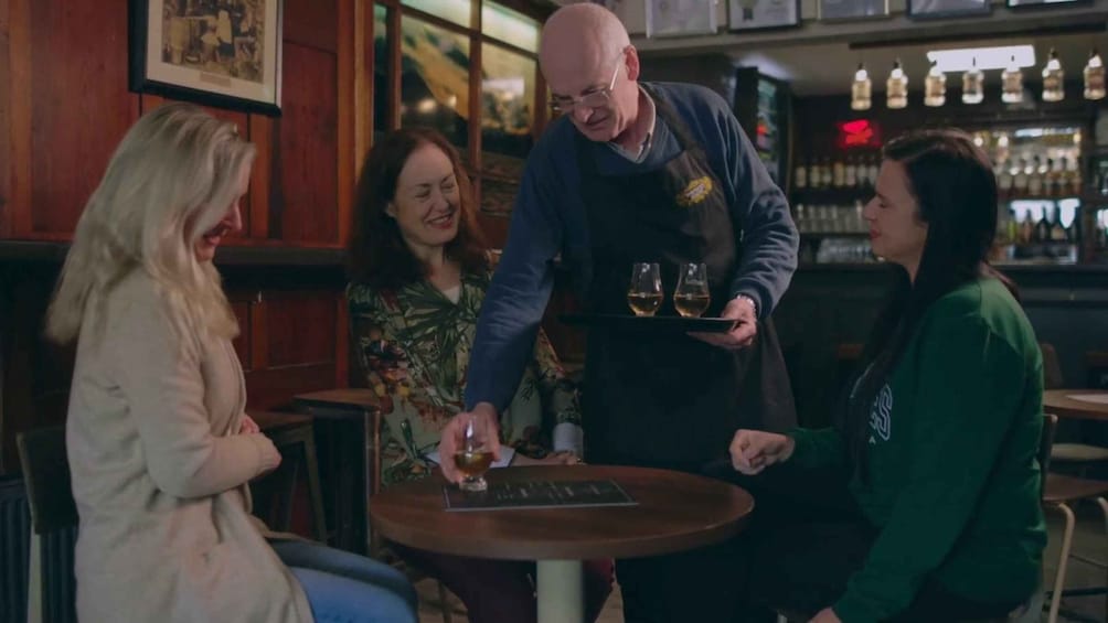 A bar setting with a bartender serving drinks to customers seated at a table. 4