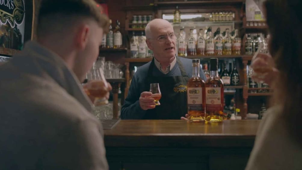 A bar with a bartender and customers. There are bottles and glasses on the counter. 3