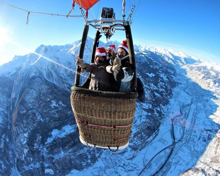 A hot air balloon with passengers wearing Santa hats, flying over a snowy mountainous landscape. 2