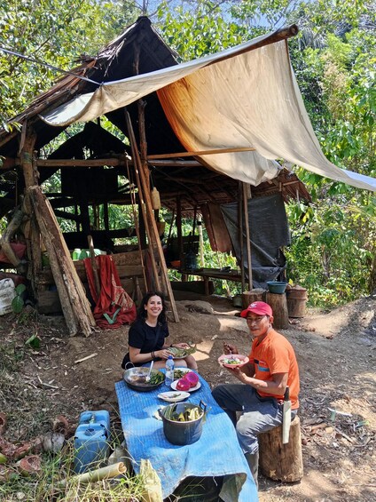 Two people sitting at a table outdoors with a makeshift shelter in the background. 5