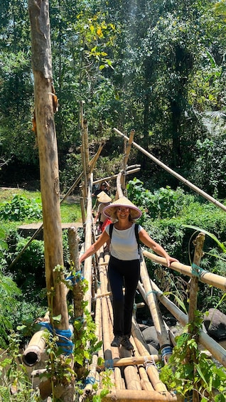 A person crossing a bamboo bridge in a lush, green environment. 1
