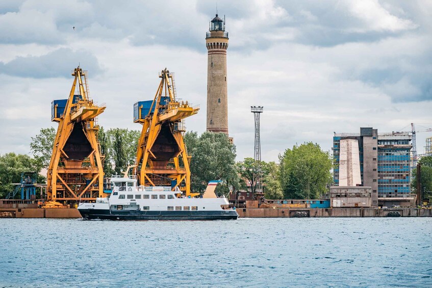 A river with a large ship docked, a lighthouse, and industrial cranes. 5