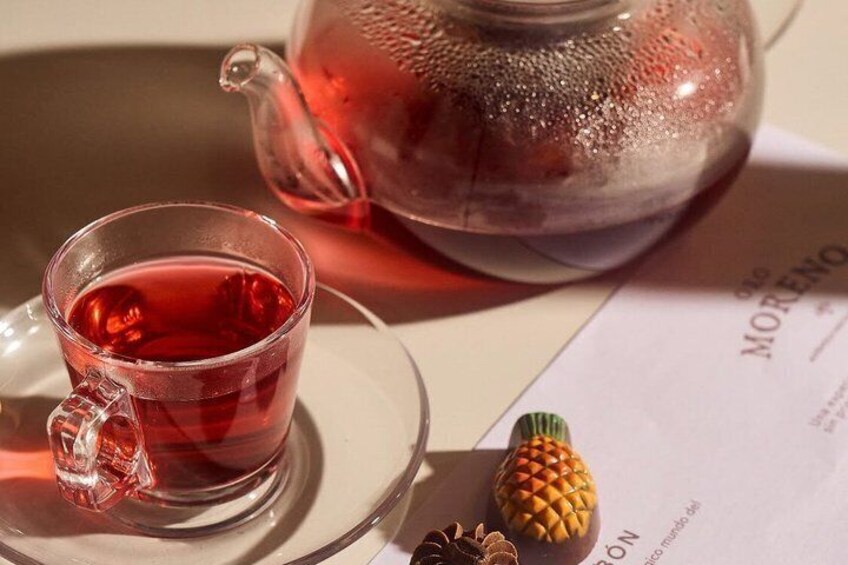 A clear glass cup of red tea, a glass teapot, and a menu with a pineapple decoration. 5