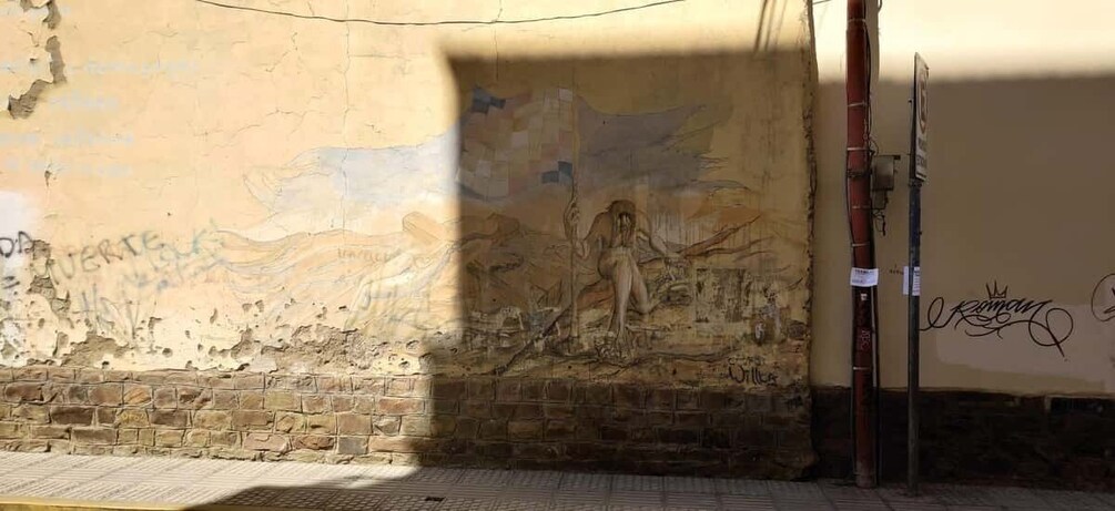 A weathered wall with graffiti and a mural. 1