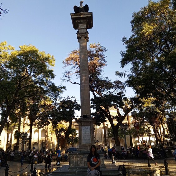 A tall monument with an eagle statue on top, surrounded by trees and people in a park. 3