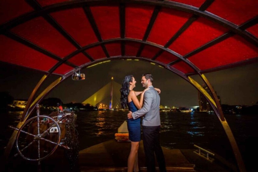 A couple embracing under a red canopy on a boat with a city skyline in the background. 2