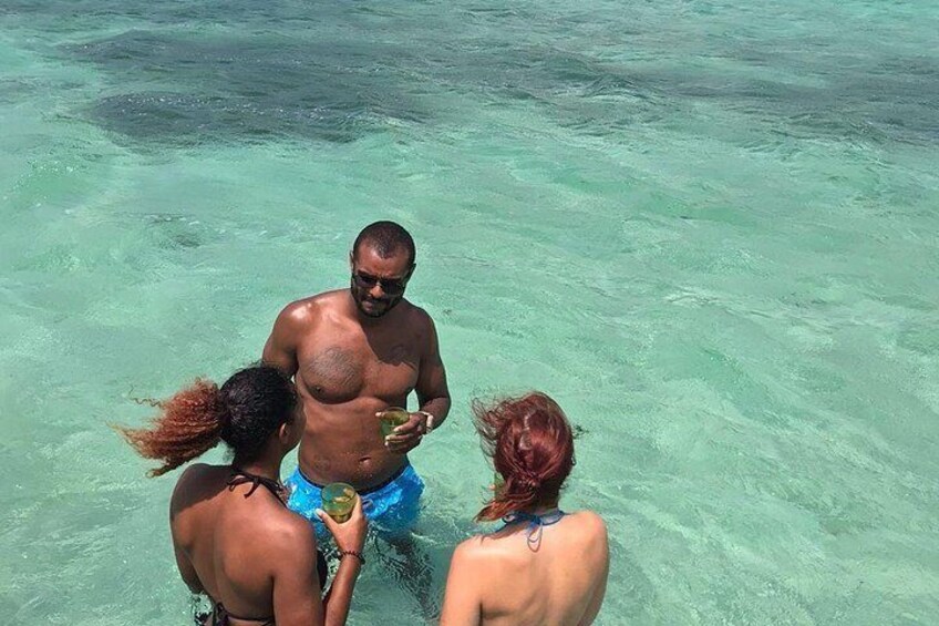 Three people in shallow water, one holding a drink. 4
