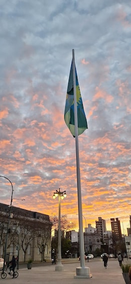 A flagpole with a flag, street lamps, buildings, and a sunset sky. 2