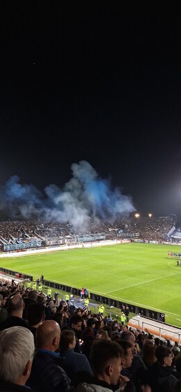A stadium filled with spectators, a soccer field, and smoke rising from the stands. 3
