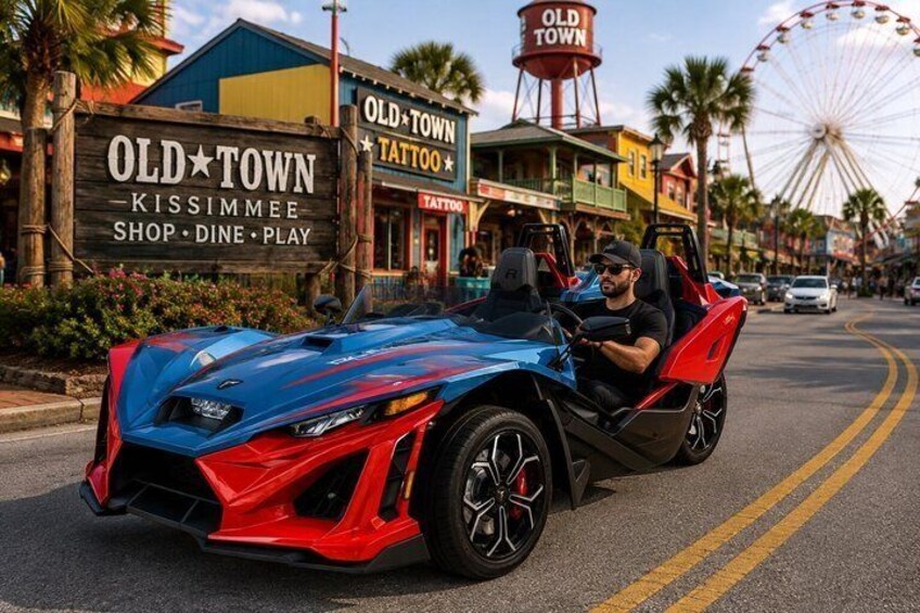 A red and blue sports car driving on a street with palm trees and a Ferris wheel in the background. 1