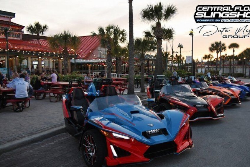 A row of sports cars parked outdoors, palm trees, and a building with a red roof in the background. 5