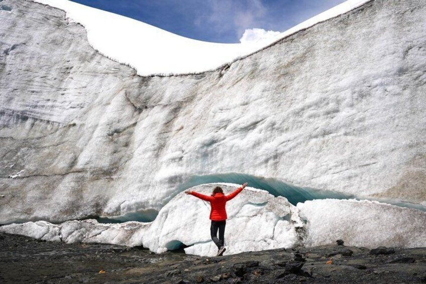 A person standing in front of a glacier with arms raised. 1