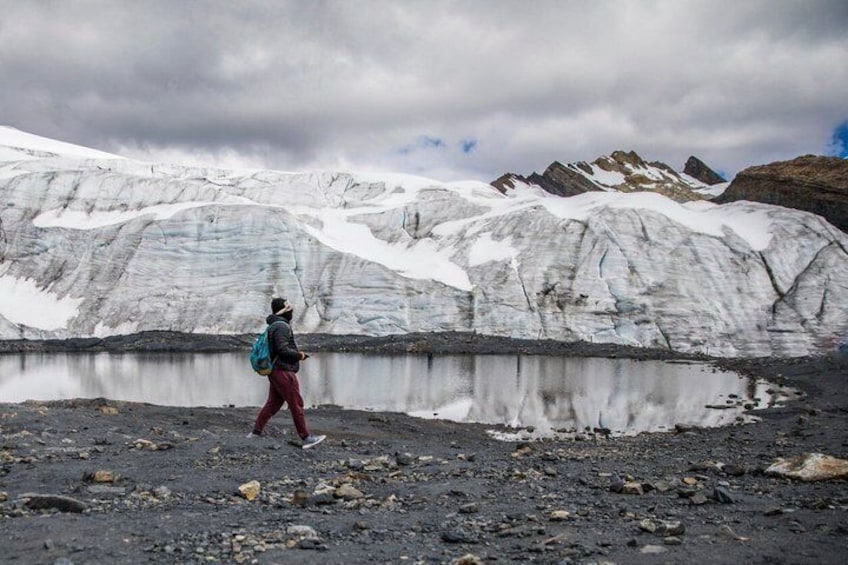 A person walking near a glacier with a lake in the foreground. 4