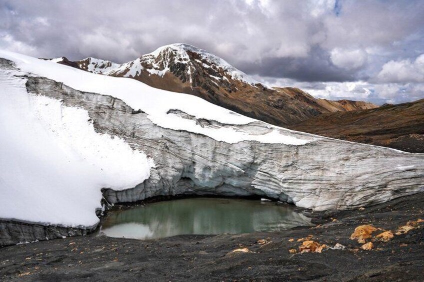 A glacier with a crevasse and a small pond, surrounded by mountains and snow. 3