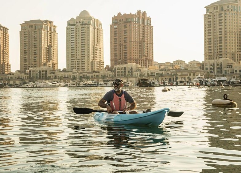 A man in a kayak on a calm body of water with a cityscape in the background. 4