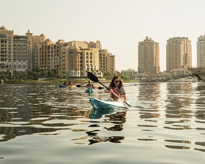 A person kayaking on a calm body of water with buildings in the background. 2