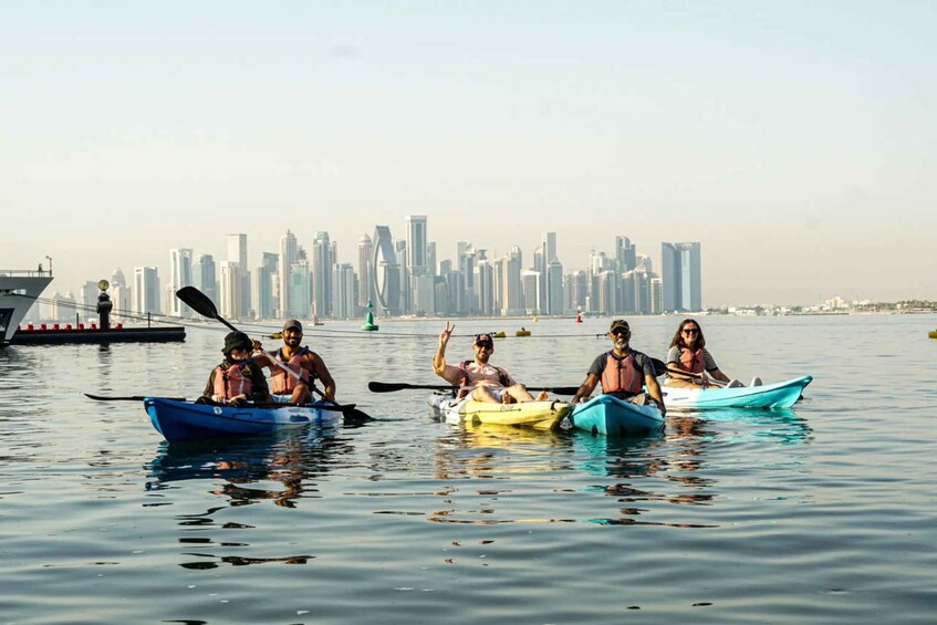 A group of people kayaking on a calm body of water with a city skyline in the background. 1
