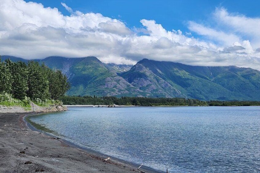A lake with mountains in the background, a sandy beach, and a clear sky. 1