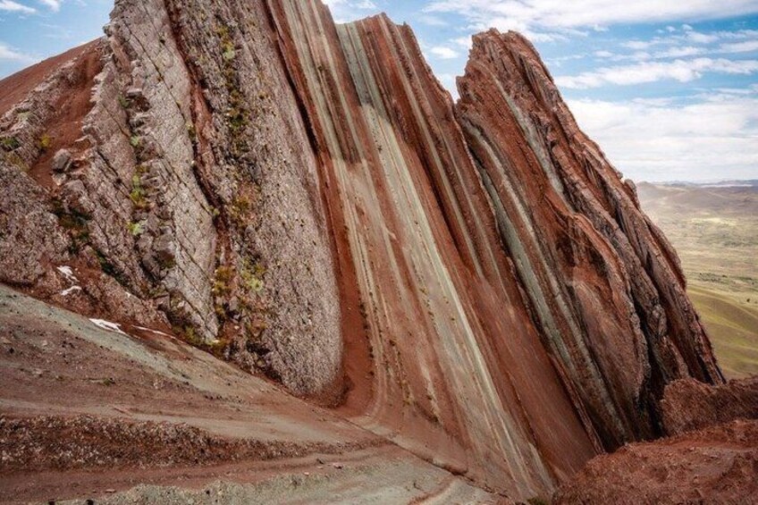 A large rock formation with striations and a dirt path leading up to it. 2