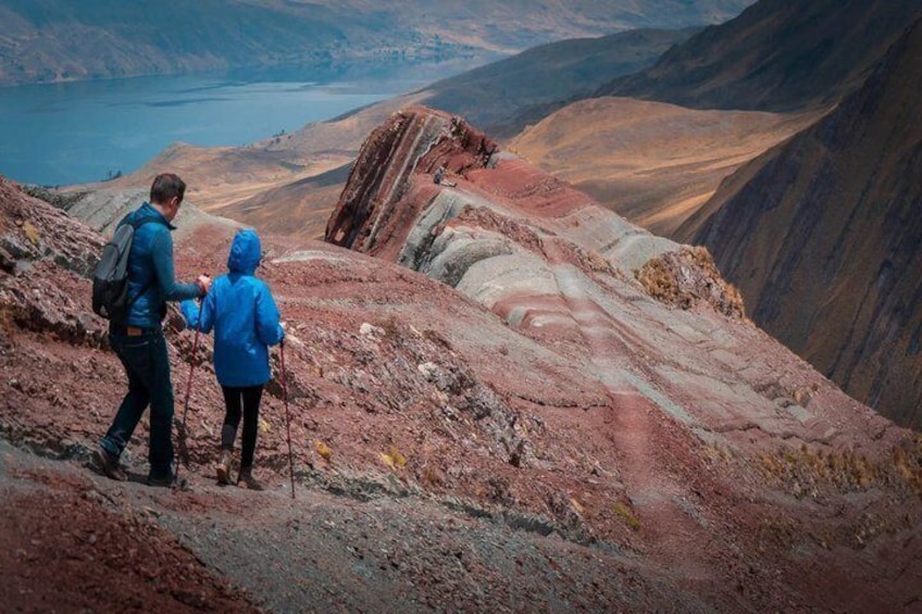 Two people hiking on a rocky mountain trail with a lake in the background. 1