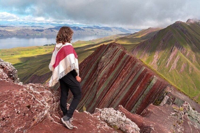 A person standing on a rocky outcrop overlooking a mountainous landscape with a lake in the distance. 4