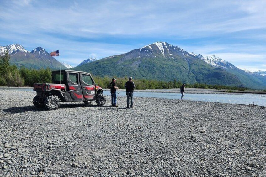 A red off-road vehicle on a gravel beach with mountains in the background. 5