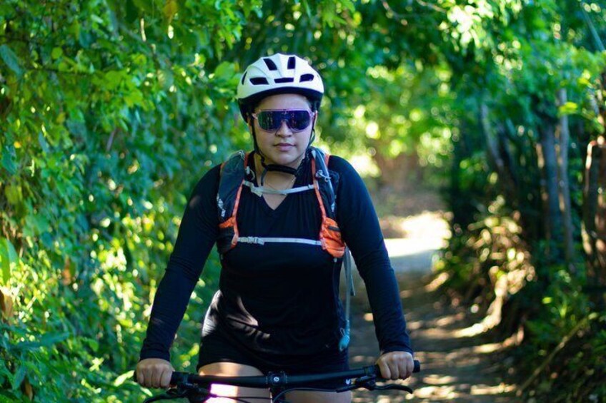 A person riding a bicycle on a narrow path surrounded by dense green foliage. 3