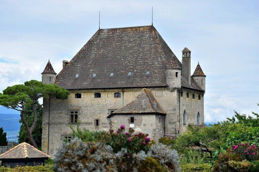 A historic stone building with a steeply pitched roof, multiple chimneys, and a tower. 3