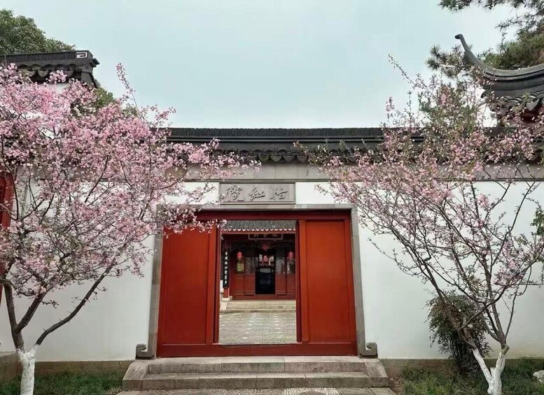 A traditional building entrance with a red door, surrounded by cherry blossom trees. 1