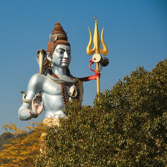 A large statue of a deity with a trident, surrounded by dense foliage. 2