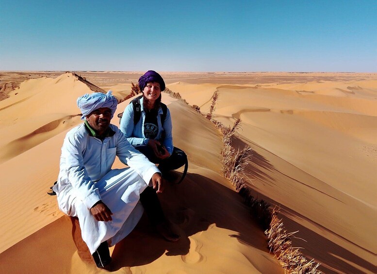 Two people sitting on a sand dune in a desert landscape. 2