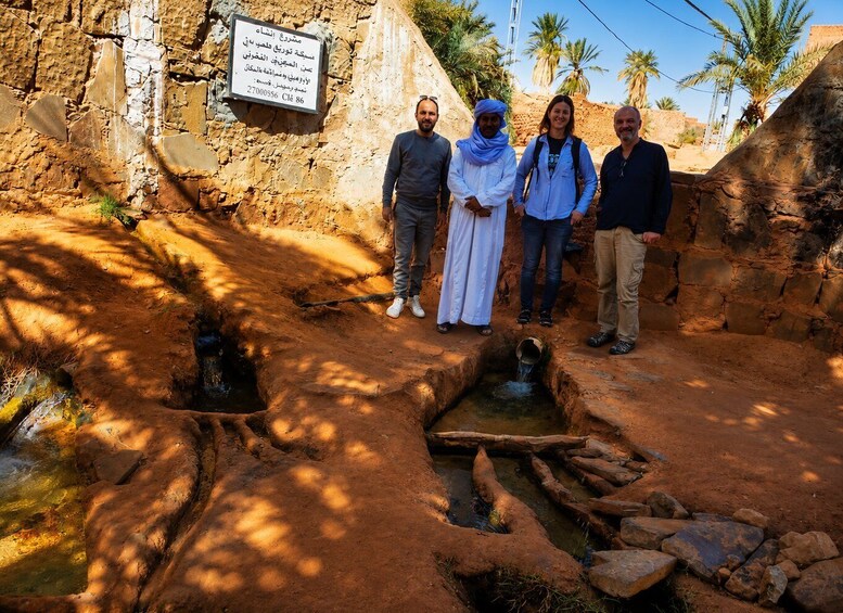 A group of people standing near an ancient stone structure with a small water channel. 1