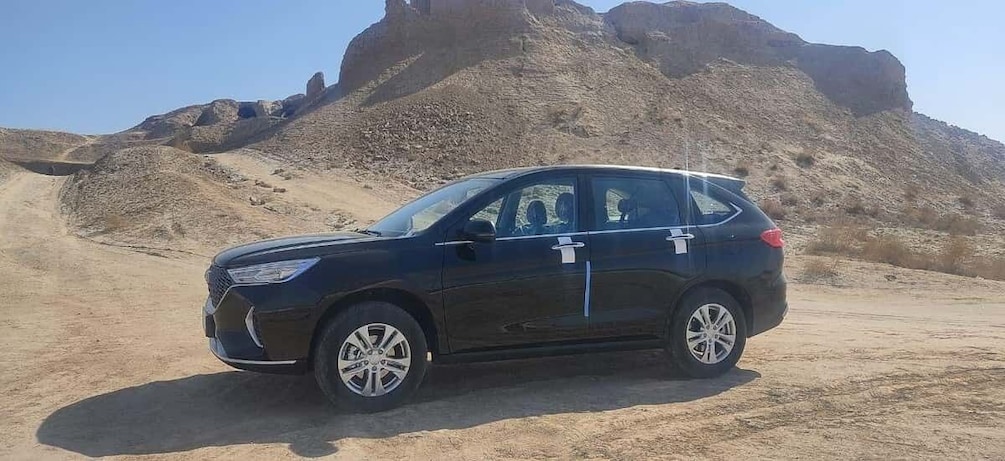 A black SUV parked on a dirt road with a rocky desert landscape in the background. 5
