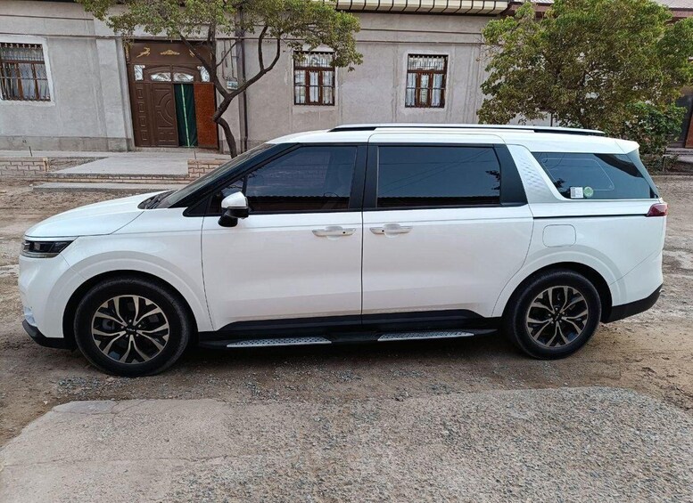 A white SUV parked on a gravel surface in front of a building with a brown door and windows. 1