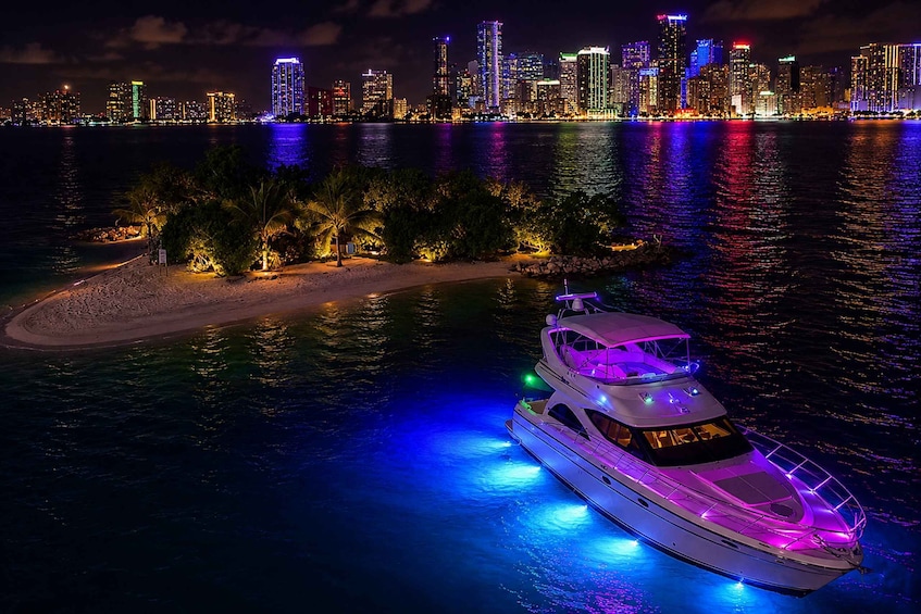 A yacht with colorful lights anchored near a beach with palm trees, with a city skyline in the background. 1