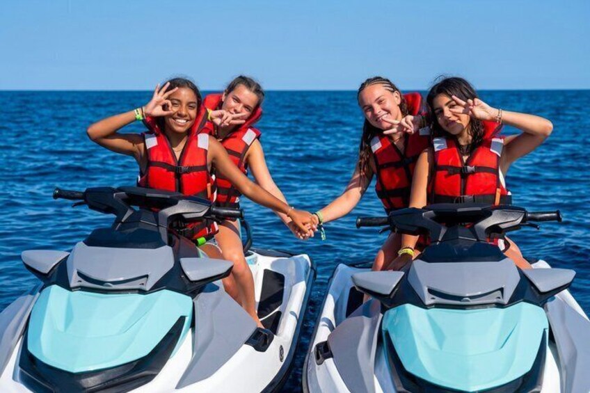 Four people on jet skis, wearing life jackets, on a body of water. 4