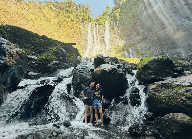 Two people standing in front of a waterfall with a forested hillside in the background. 3
