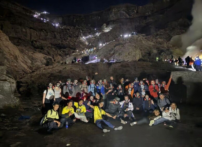A group of people gathered in a rocky outdoor setting at night, with artificial lighting illuminating the area. 3