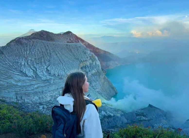 A person standing on a mountain overlooking a valley with a view of a volcano and clouds. 2