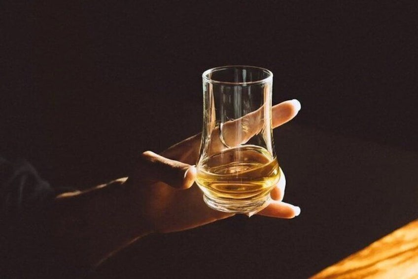 A hand holding a glass of amber liquid, likely a beverage, against a dark background. 2