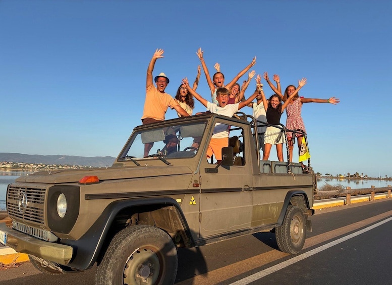A group of people on a vehicle with raised arms, a clear sky, and a body of water in the background. 1