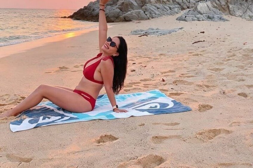 A person in a red bikini lying on a towel on a sandy beach with rocks in the background. 4
