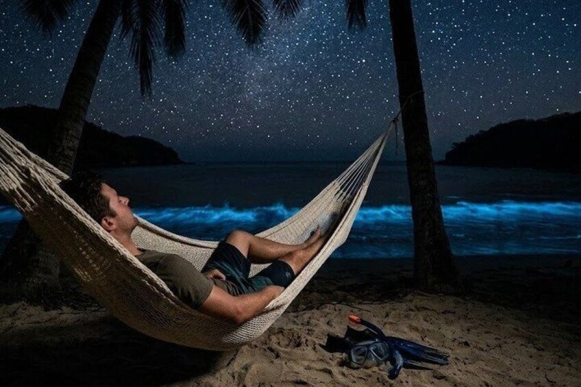 A person relaxing in a hammock on a beach at night with stars visible in the sky. 1