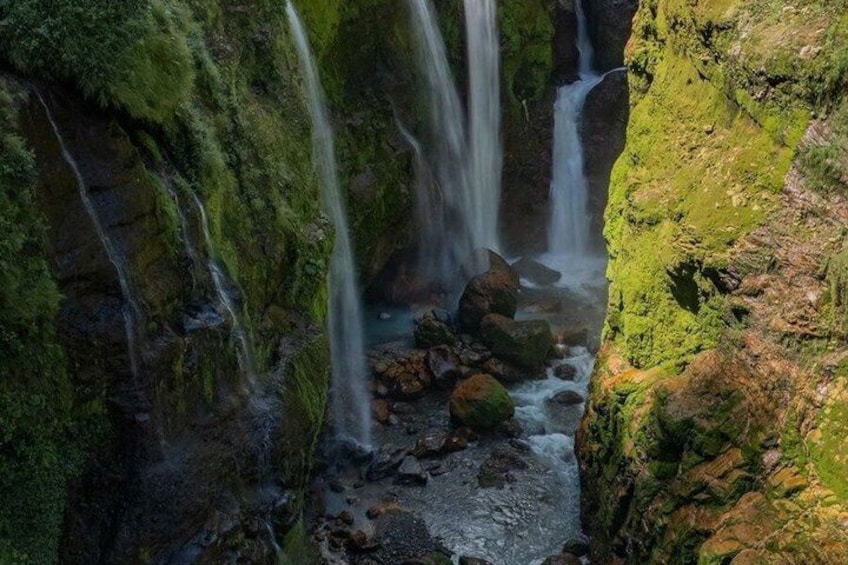 A waterfall cascading over moss-covered rocks in a narrow gorge. 1