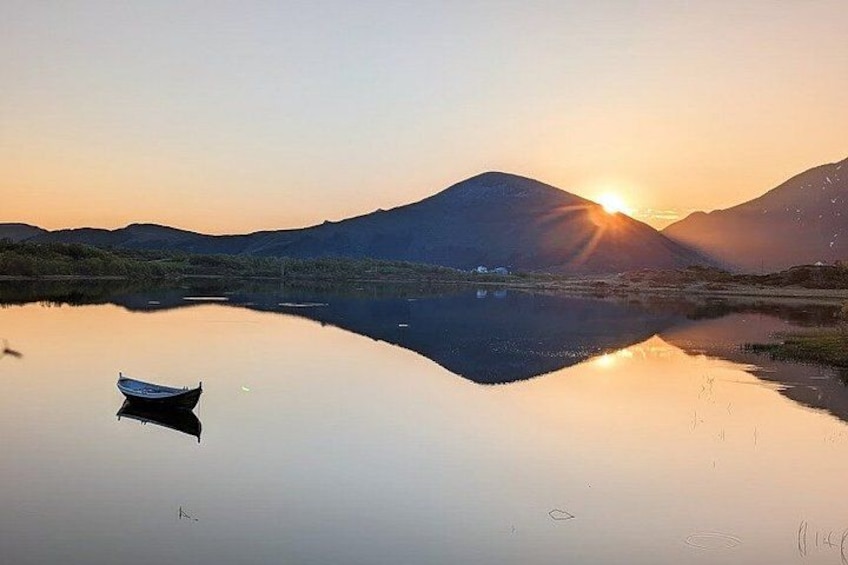 A calm lake with a boat, mountains, and a setting sun. 1