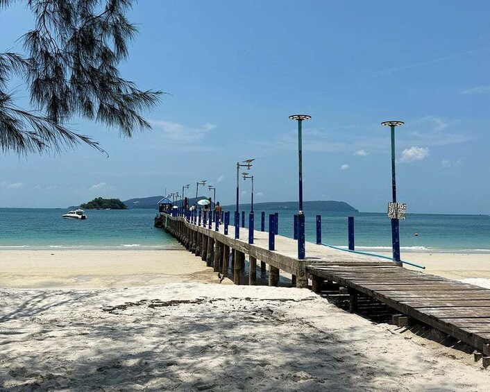 A beach with a wooden pier extending into the ocean, a boat on the water, and a clear blue sky. 3