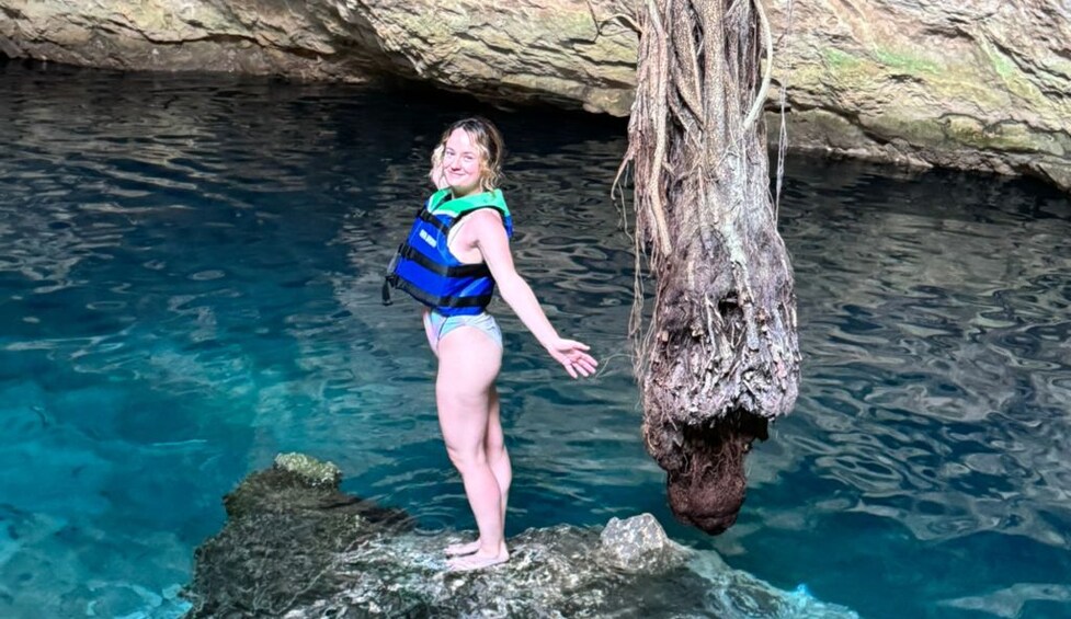 A person standing on a rock in a cave with clear blue water. 3